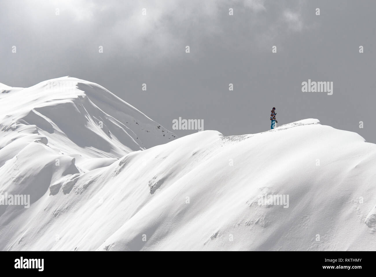 A stranded man on the snowy ridge of a mountain holding a cell phone trying to call Stock Photo