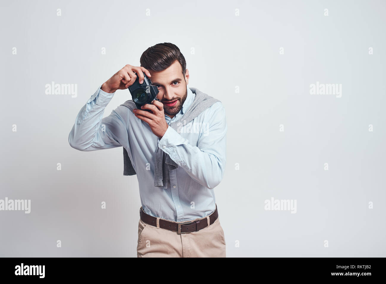 Nice shot. Attractive young man in casual wear is photographing you while standing in studio on a grey background. Close-up portrait Stock Photo