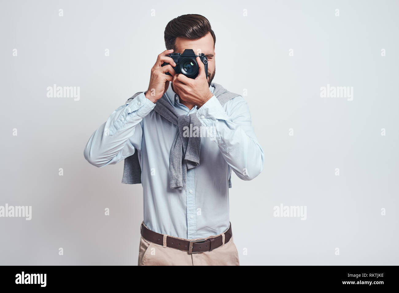 Do what you love. Young bearded man in blue shirt taking picture with camera isolated on grey background. Close-up picture Stock Photo