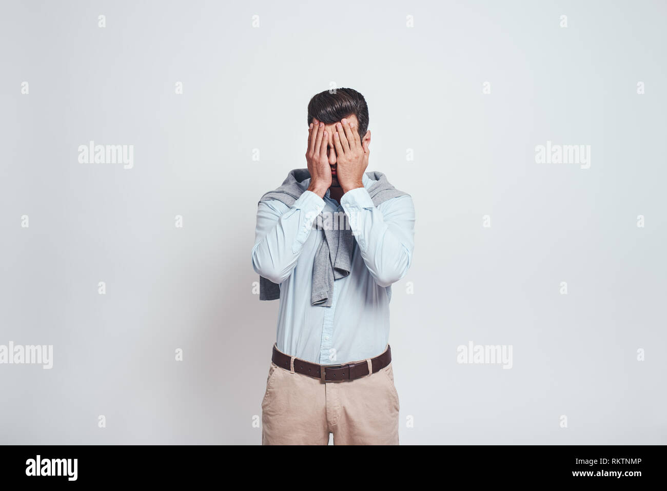 What did i do. Close-up portrait of disappointed man closing eyes with his hands on a grey background. Stress concept. Emotion expression. Stock Photo