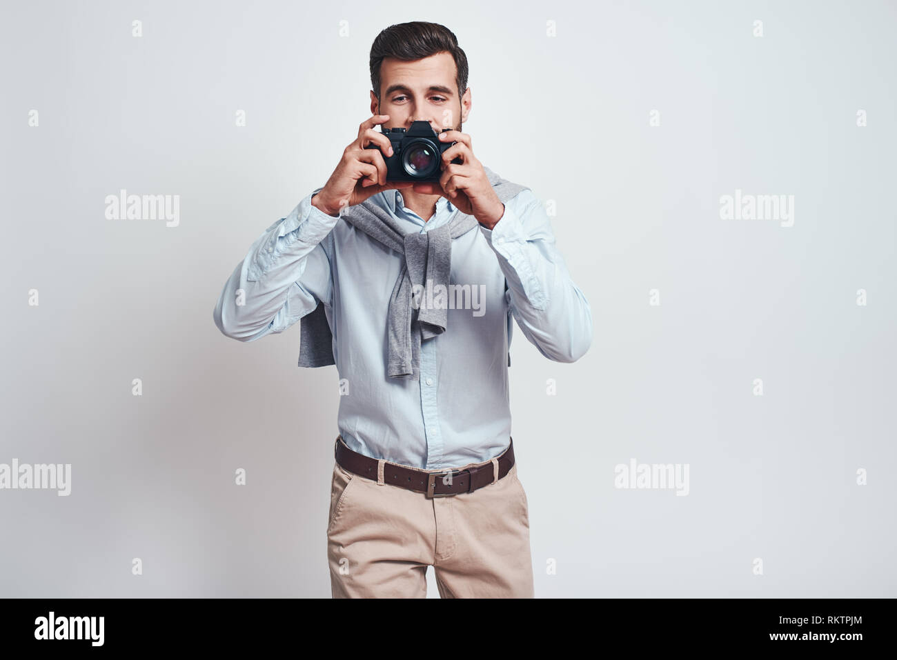 Smile. Close up photo of handsome male photographer in casual clothes who is taking photos with camera on the grey background. Studio portrait Stock Photo