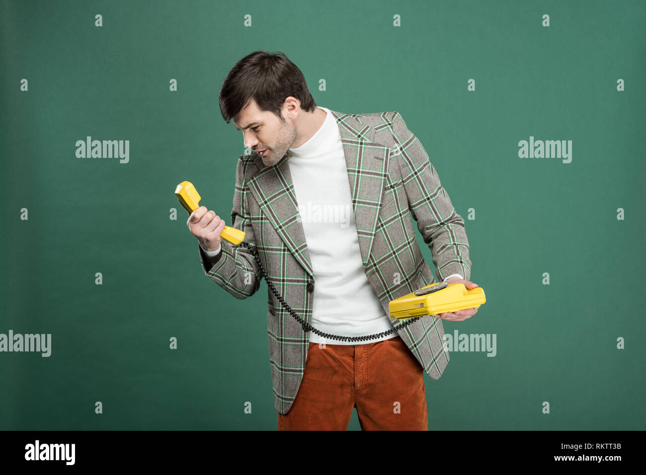 dissatisfied handsome man in vintage clothes looking at retro telephone isolated on green Stock Photo