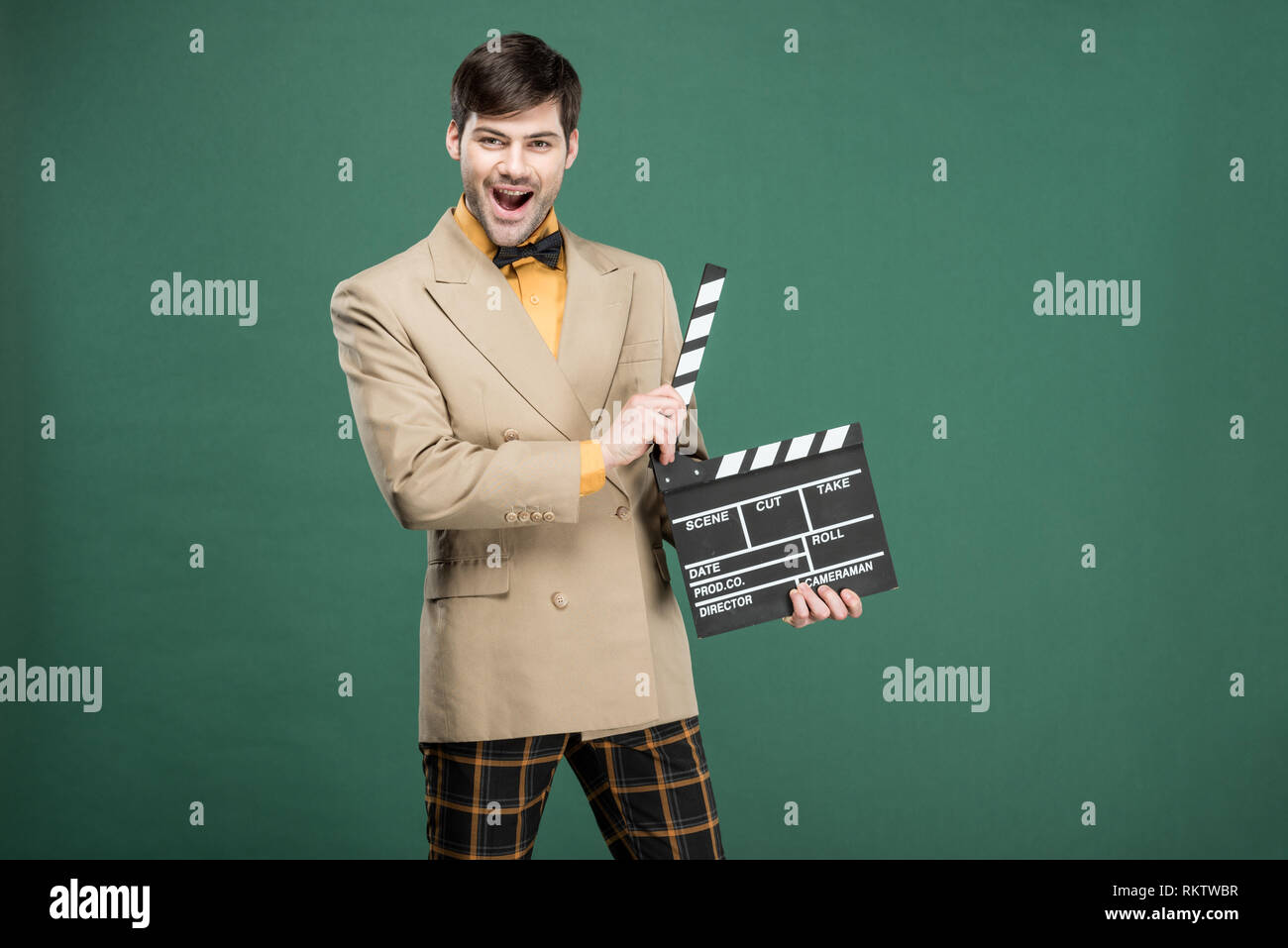 excited handsome man in vintage clothes looking at camera and holding film clapperboard isolated on green Stock Photo