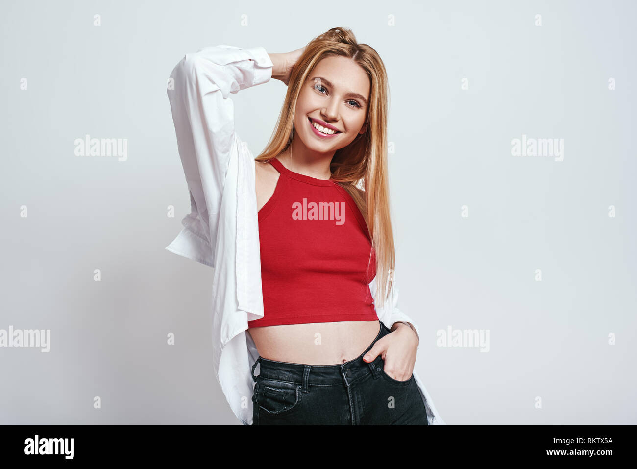 Feeling happy. Attractive young blonde woman in red tank top feeling so excited, smiling and looking at camera. Grey background. Beauty concept Stock Photo