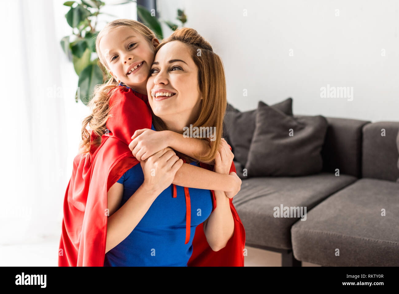daughter and mother in red cloaks hugging and smiling at home Stock Photo