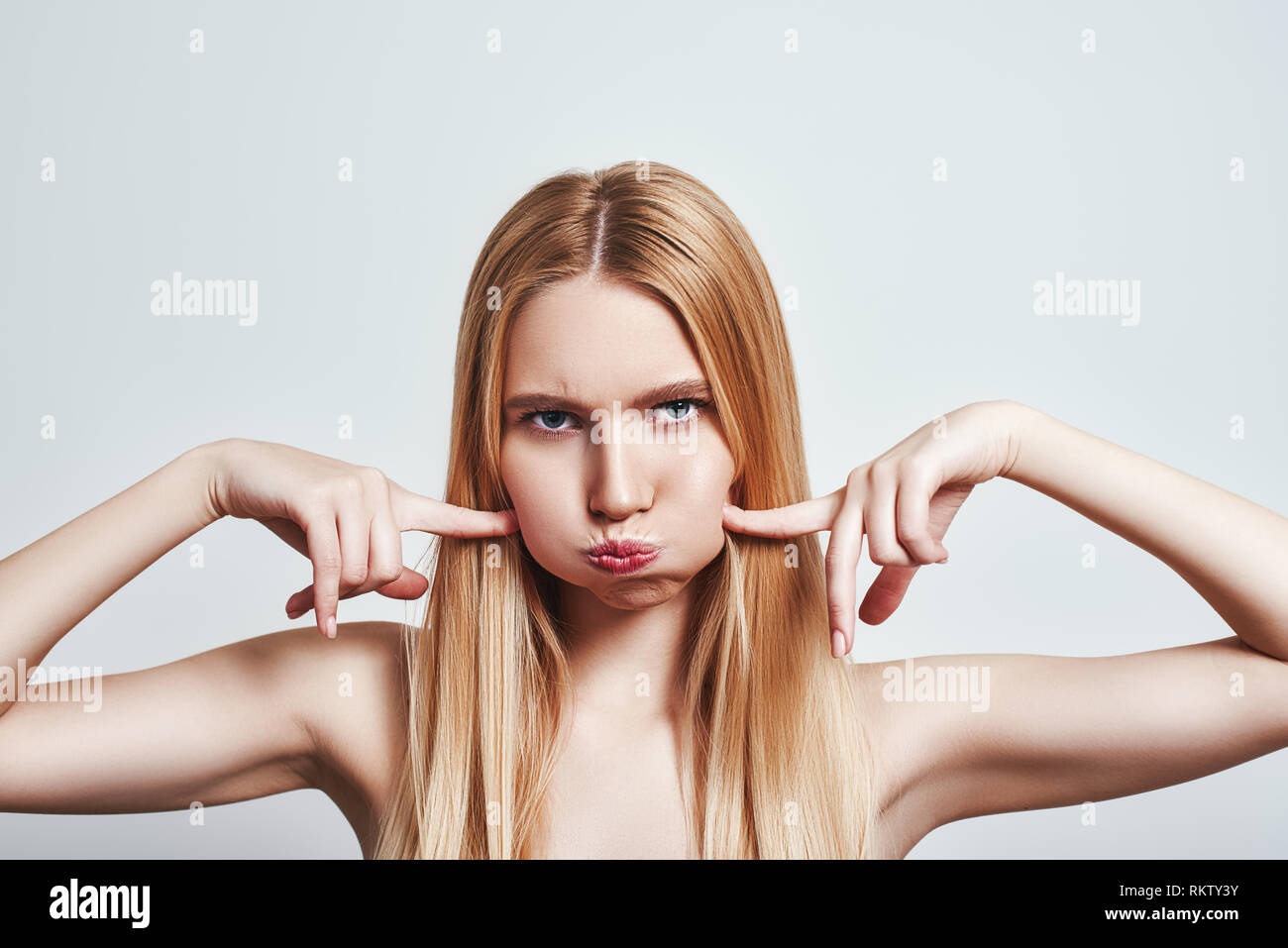 Studio shot of stubborn young blonde woman blowing cheeks and feeling mad. Human emotions. CLose-up Stock Photo