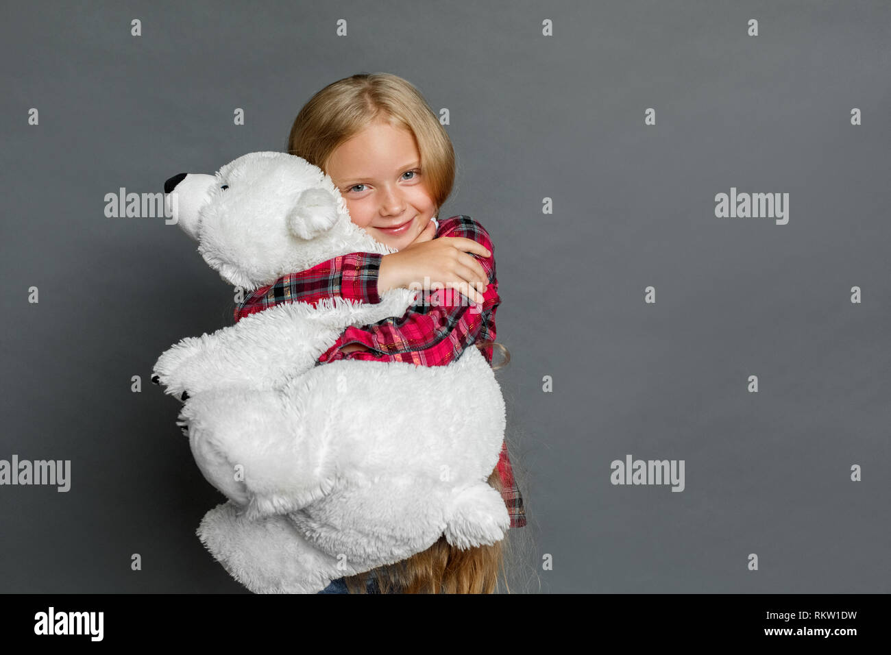 Little girl studio standing isolated on grey wall hugging teddy bear ...