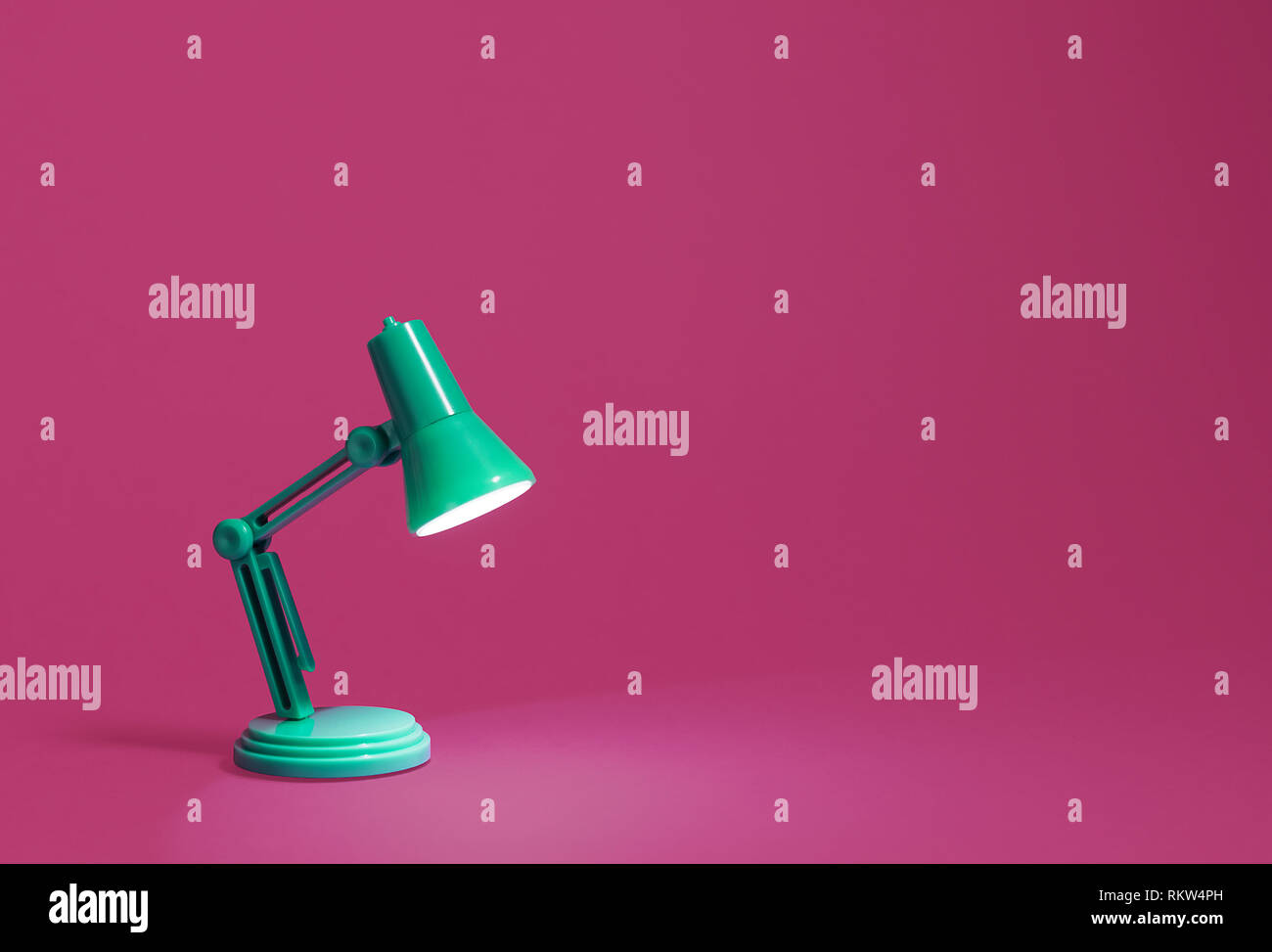 Retro green desk lamp turned on and shining onto a bright pink work surface background.  copy space and room for text Stock Photo
