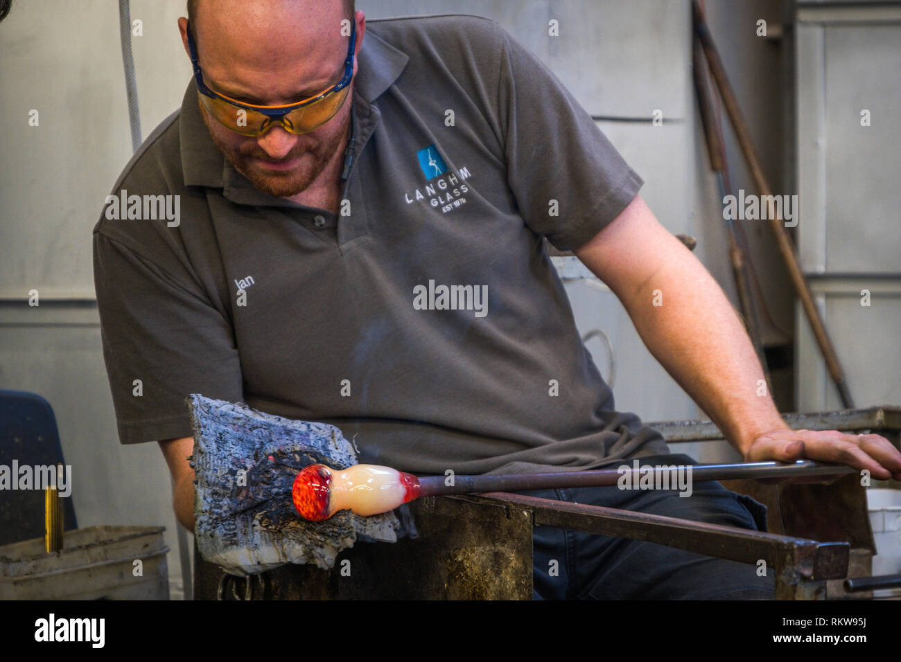 A glassblower uses a pad on a blob of molten glass to form a shape. Stock Photo