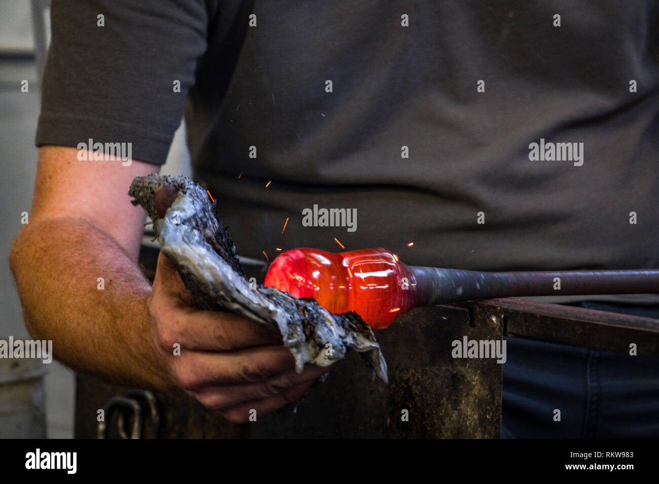 A glassblower uses a pad on a blob of molten glass to form a shape. Stock Photo