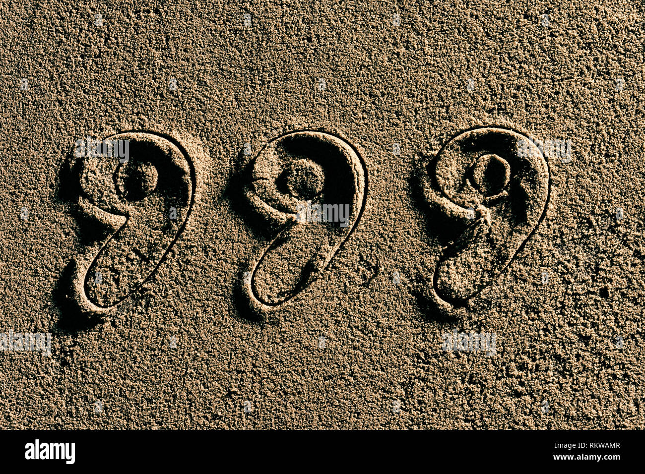 The numbers 999 cut into wet sand. Stock Photo