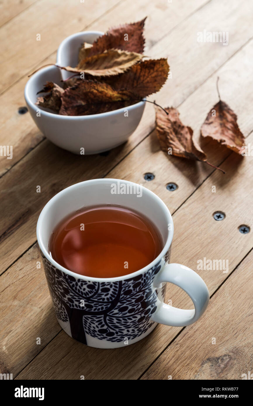 A mug of herbal tea with autumn leaves table decoration. Stock Photo