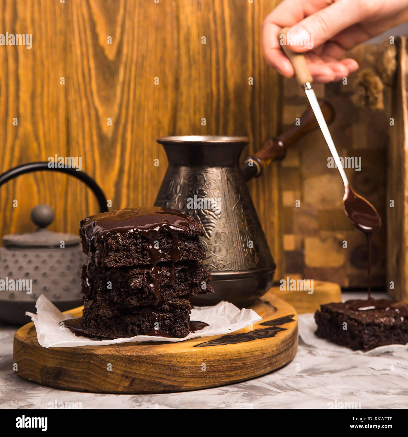 A stack of square brownie pieces poured with chocolate on a wooden board. Delicious dessert Stock Photo