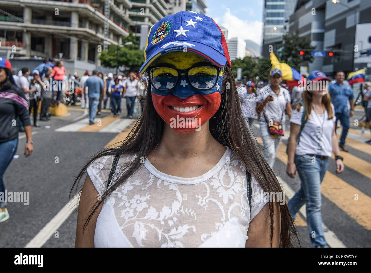 Caracas, Miranda, Venezuela. 12th Feb, 2019. A woman seen smiling at the  camera with her face painted in the venezuelan flag colors during a protest  to call for a change in the