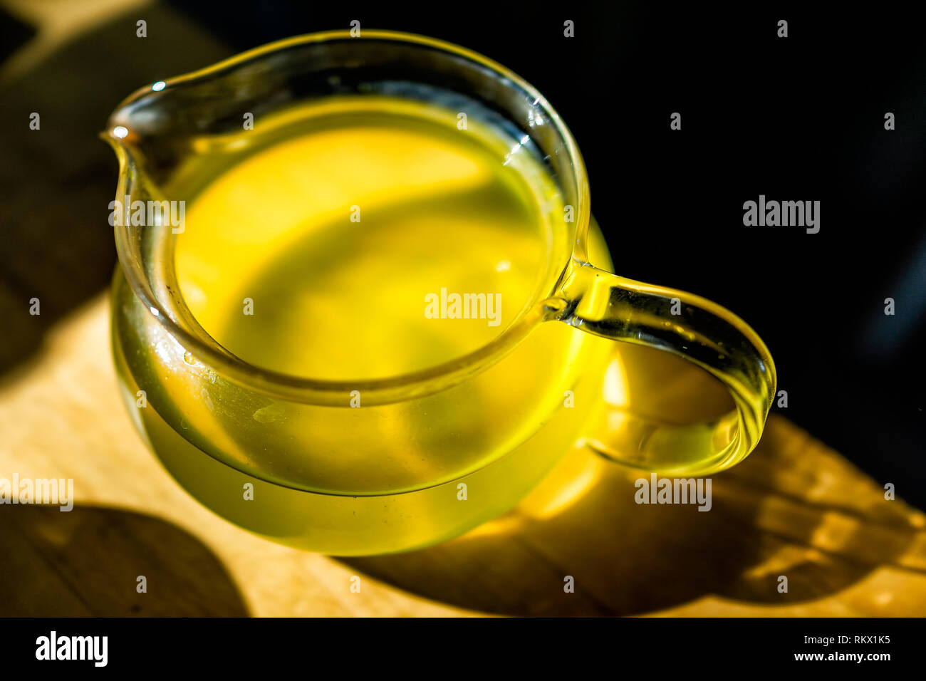 https://c8.alamy.com/comp/RKX1K5/closeup-of-glass-teapot-on-wooden-table-in-dark-room-with-sunlight-from-window-filled-with-japanese-green-or-oolong-yellow-tea-color-sencha-RKX1K5.jpg