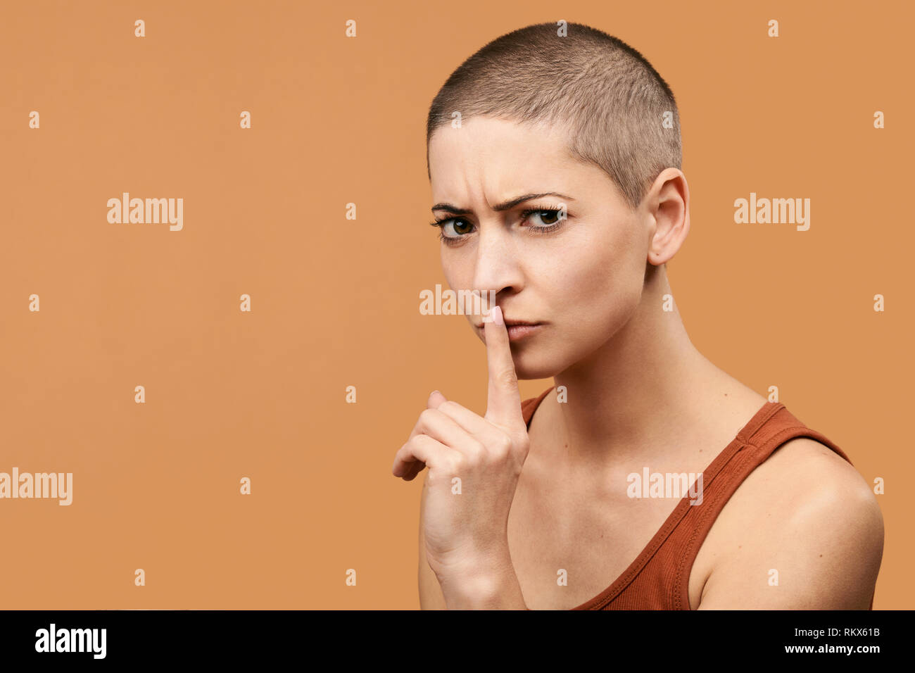 Attractive mid 30s woman pressing finger to lips as if asking to keep silent. Photo of young angry woman making Shhh gesture. Stock Photo