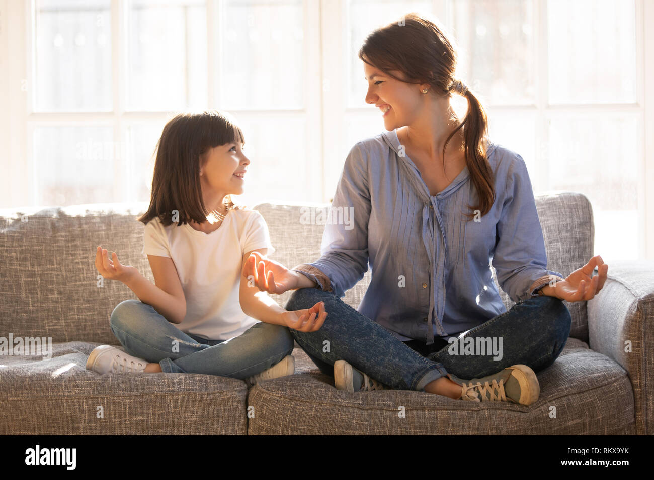 Mindful mom teaching yoga happy child daughter sitting on couch Stock Photo