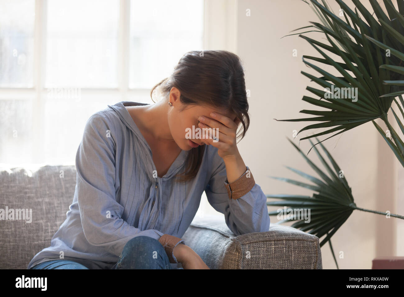 Upset depressed woman feeling tired having headache sitting on couch Stock Photo