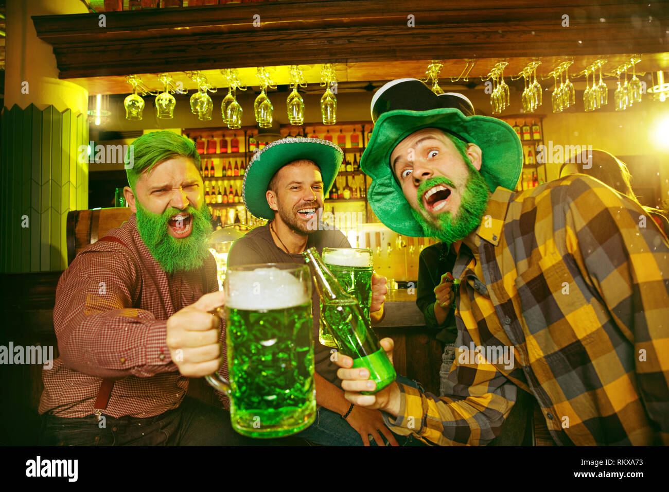 Saint Patrick's Day Party. Happy friends is celebrating and drinking green beer. Young men and women wearing a green hats. Pub Interior. Stock Photo
