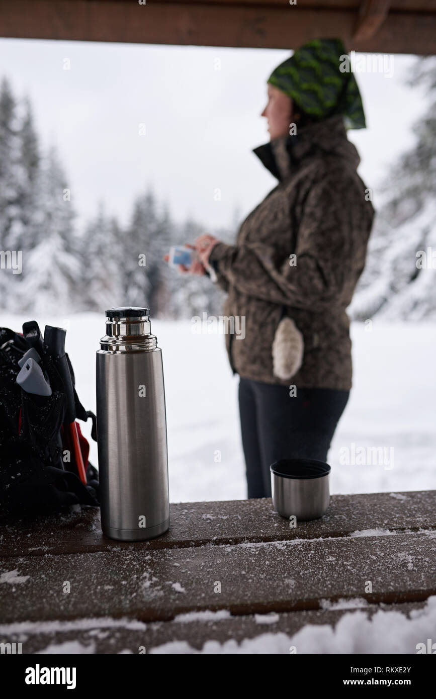 Young woman in hiking gear standing in a shelter drinking coffee while taking a break from a winter hike in a forest Stock Photo