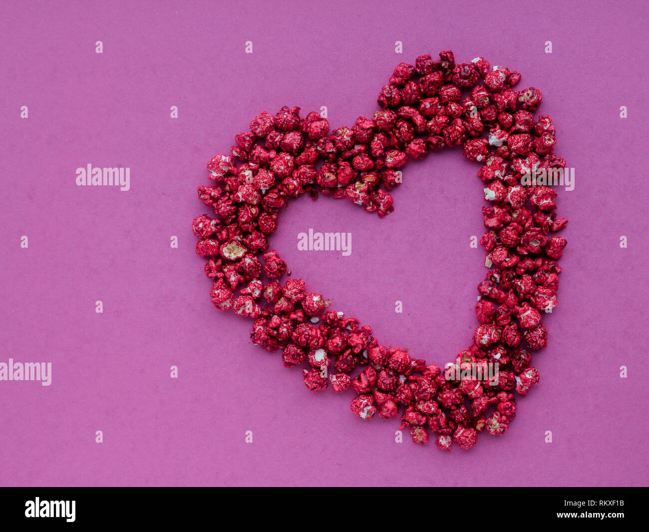 Red heart shape made from popcorn on a pink background Stock Photo