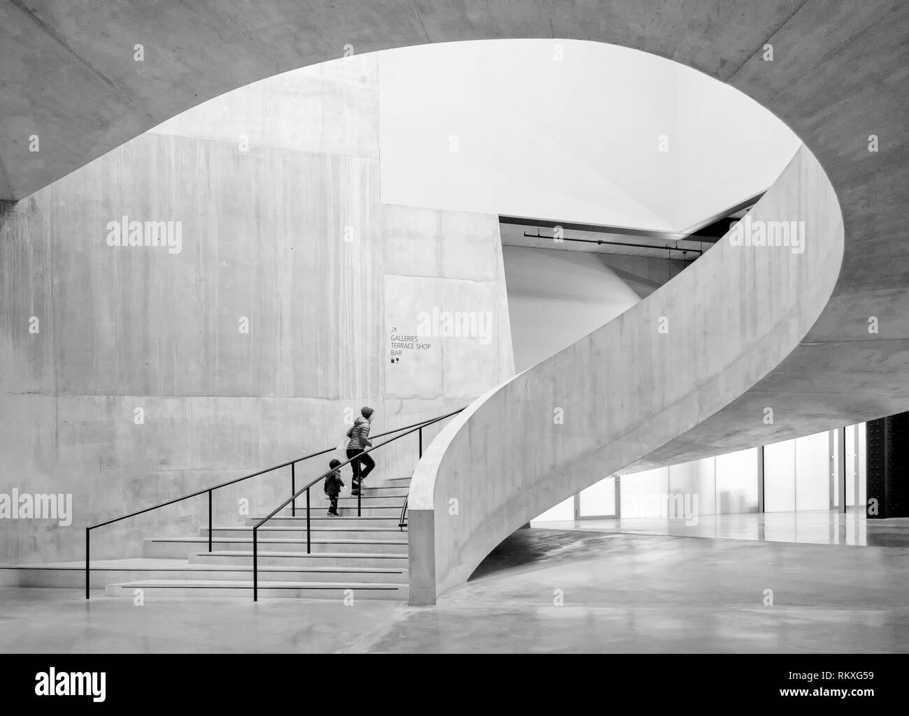 A mother and her son, a c walking up the stairs at Tate Modern in London.  This is a black & white image because it highlights the interesting shapes. Stock Photo