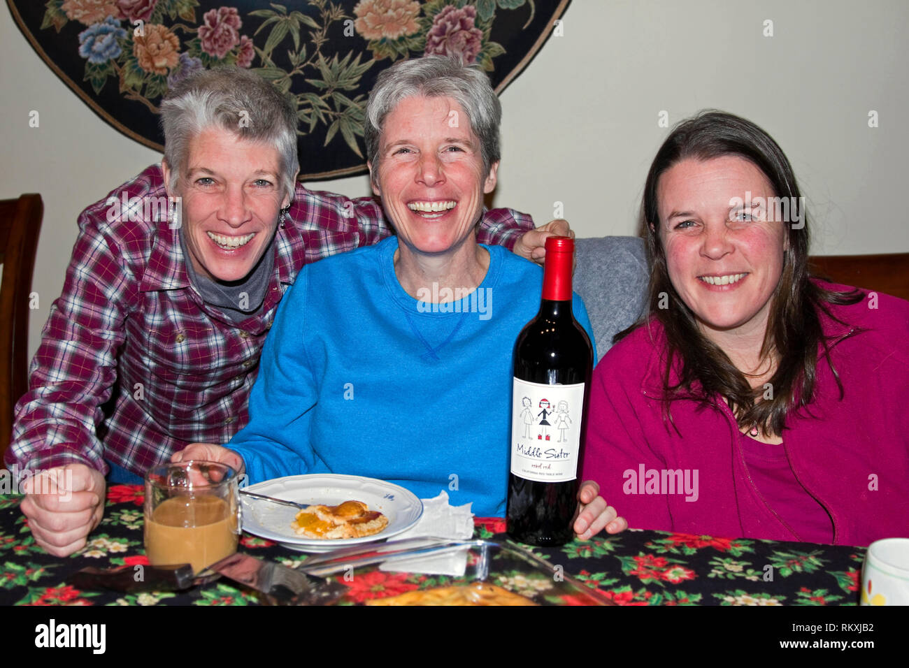 3 adult women, sisters, 40s, dinner table, wine bottle, smiling, happy, family resemblance; horizontal; MR Stock Photo