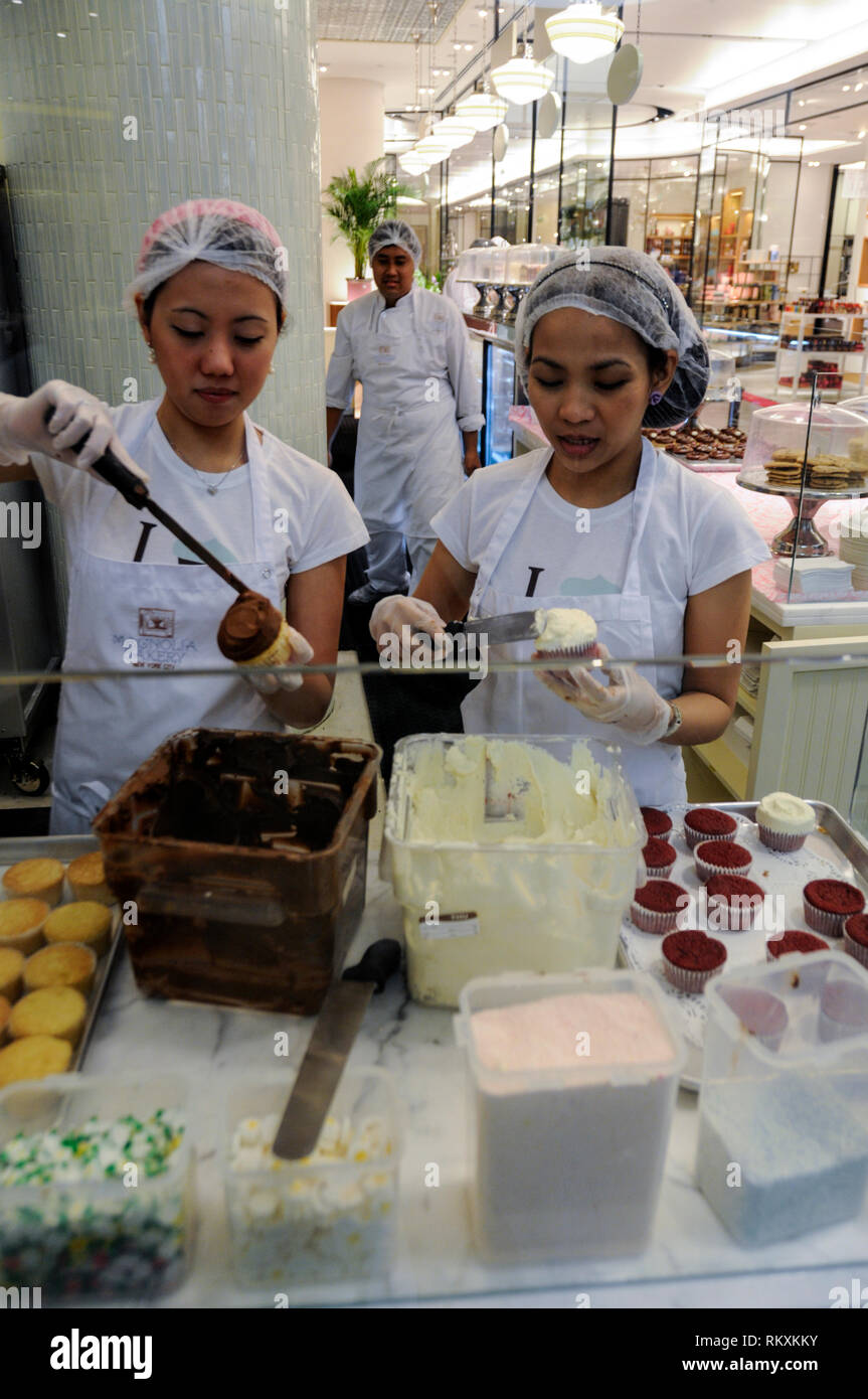 Two bakery assistances applying confectionery cream in a large bakery