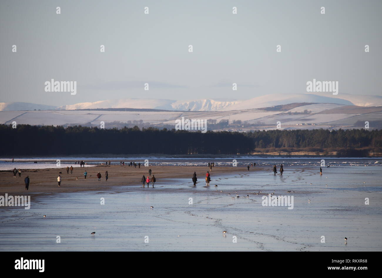 People walking on West Sands beach St Andrews with distant snow covered peaks in the Angus Glens St Andrews Fife Scotland  February 2019 Stock Photo