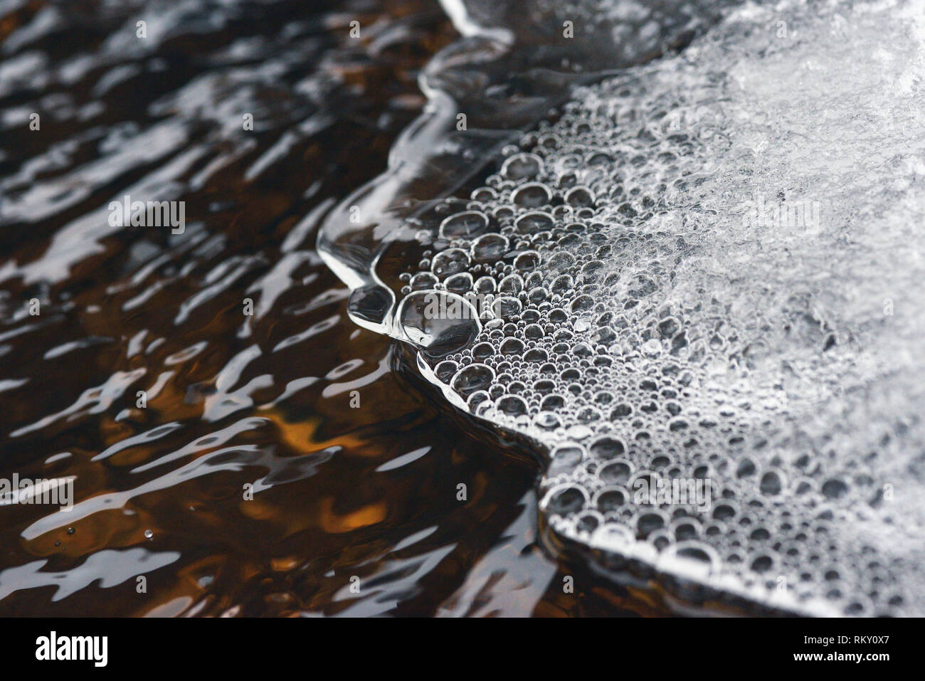 The accumulation of air bubbles under the thin crust of ice against the background of a turbulent flow of water. Stock Photo