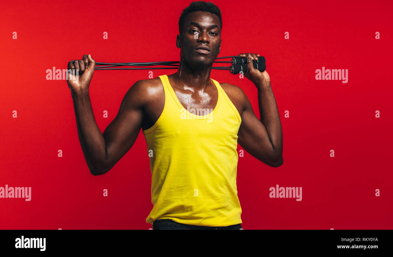 Muscular man posing with jumping rope on red background. African fitness model with skipping rope. Stock Photo