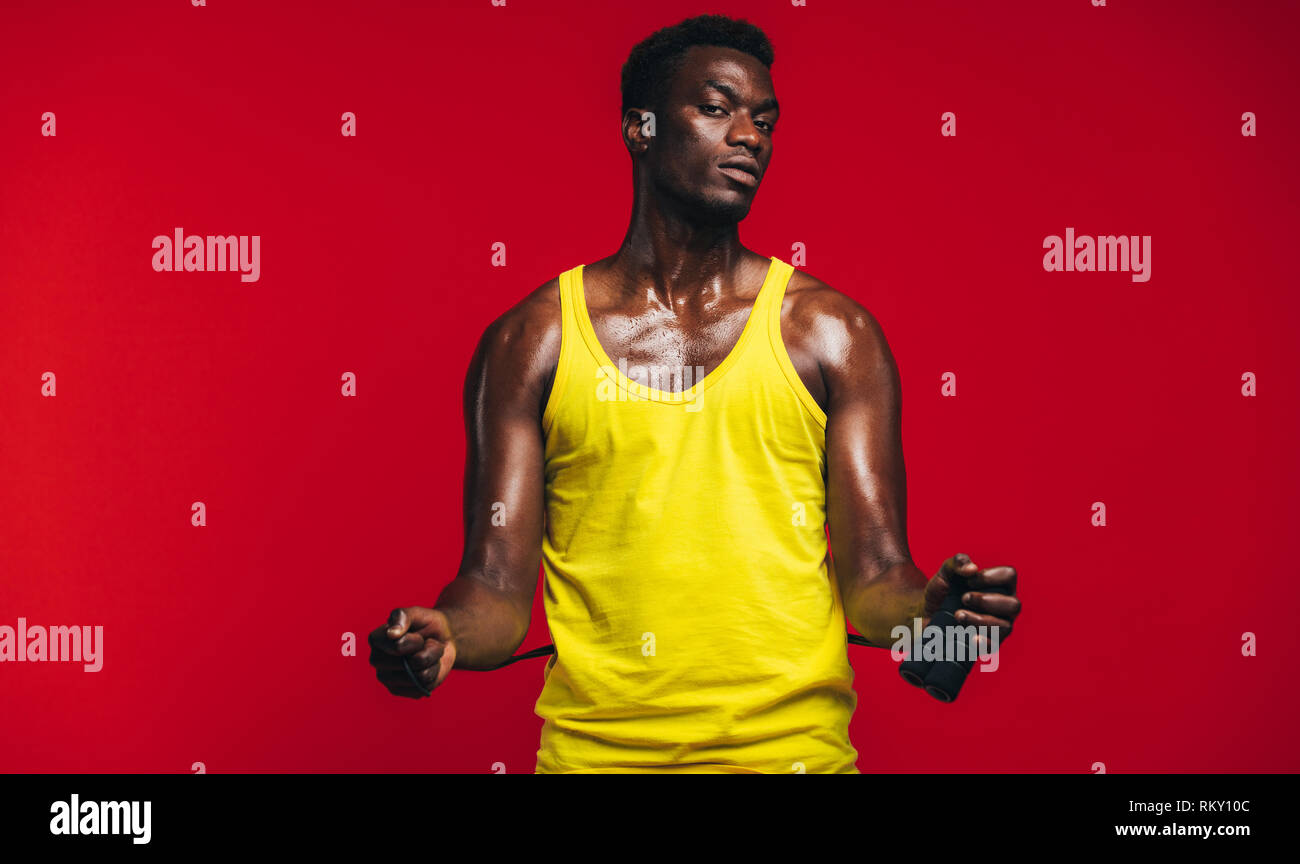 Fit young man with jumping rope on red background. African fitness male model with skipping rope looking at camera. Stock Photo