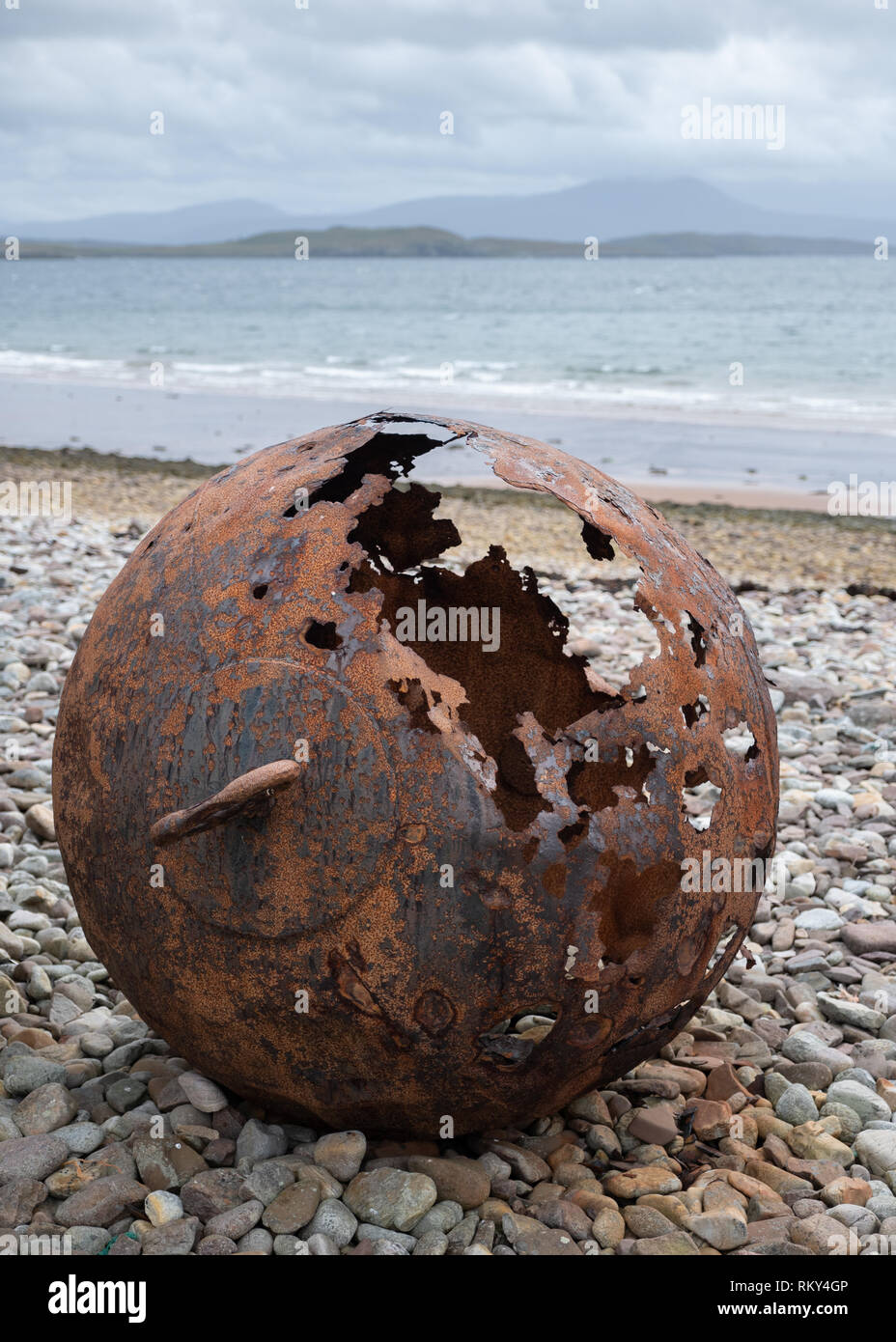 An old and rusty buoy stranded on a pebble beach near the shoreline on a cloudy day at Achiltibuie, Ross and Cromarty, Scotland Stock Photo