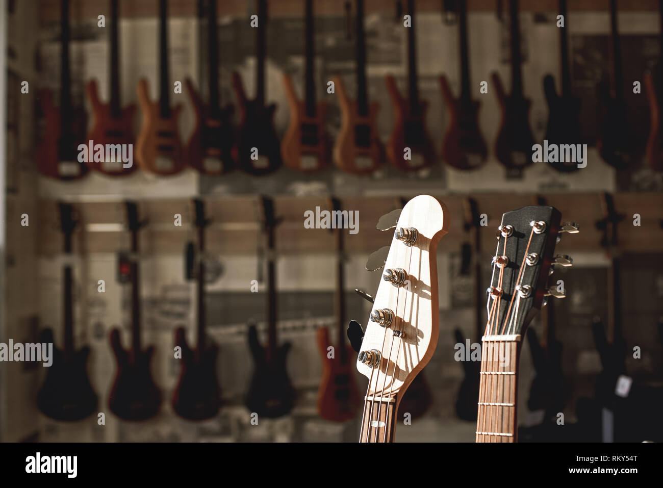Close-up view of two guitar headstocks againt of a row of different electric guitars aligned in a music store showroom. Musical instruments. Music store. Guitar body Stock Photo