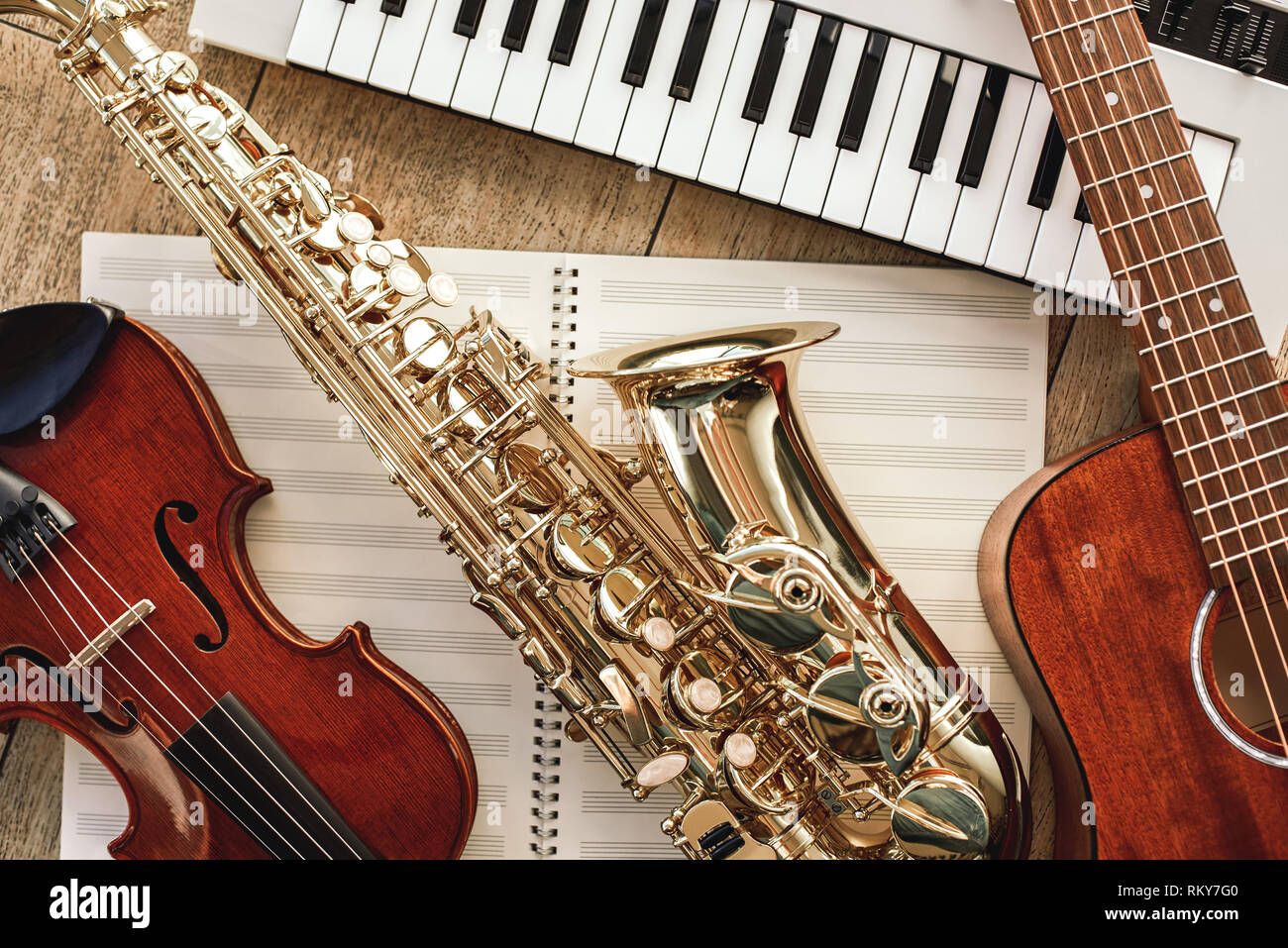 Power of music. Top view of musical instruments set: synthesizer, guitar, saxophone and violin lying on the sheets for music notes over wooden floor. Musical instruments. Music equipment Stock Photo