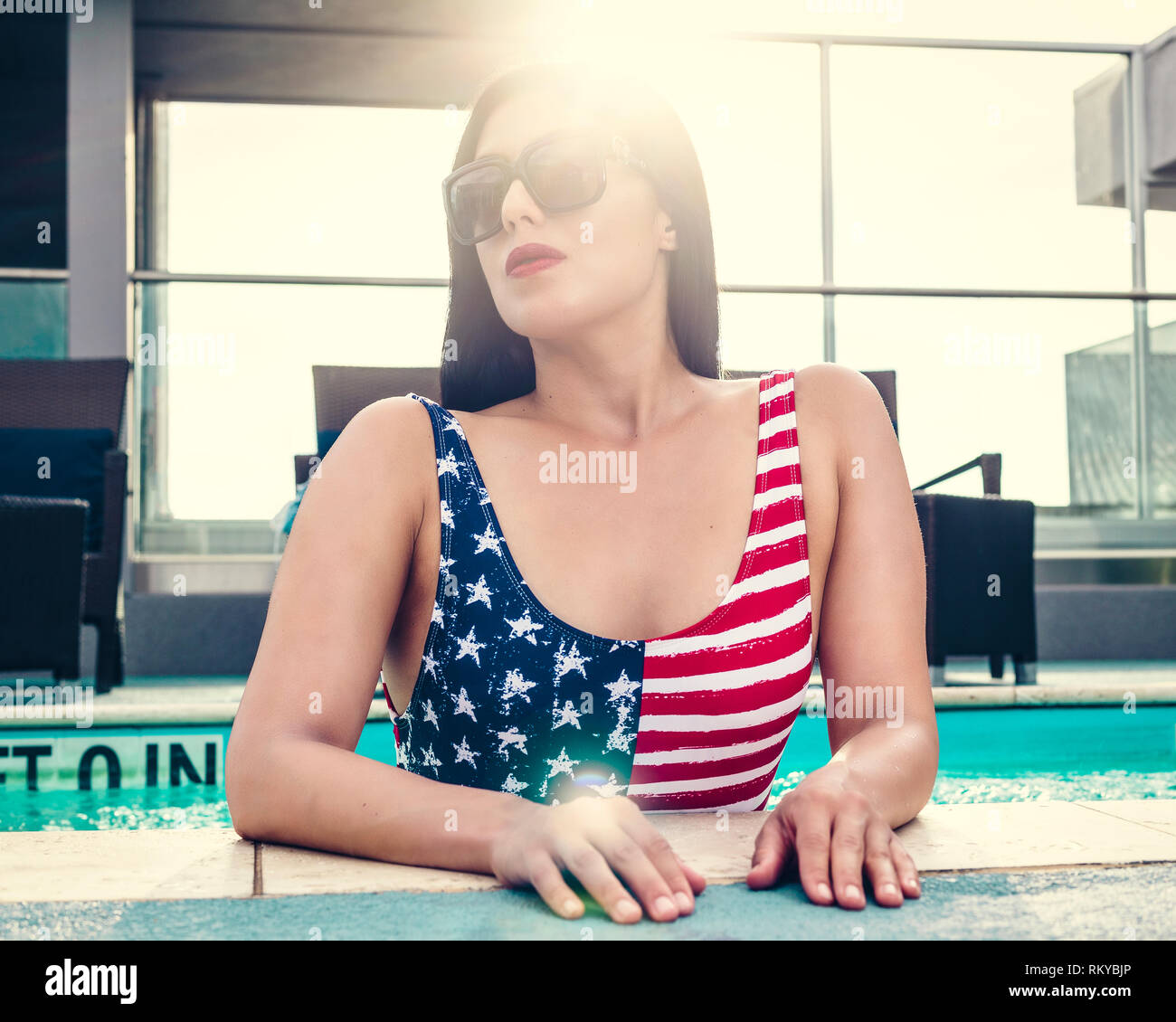 Swimsuit model in American Flag swimsuit in pool with sunglasses. Stock Photo
