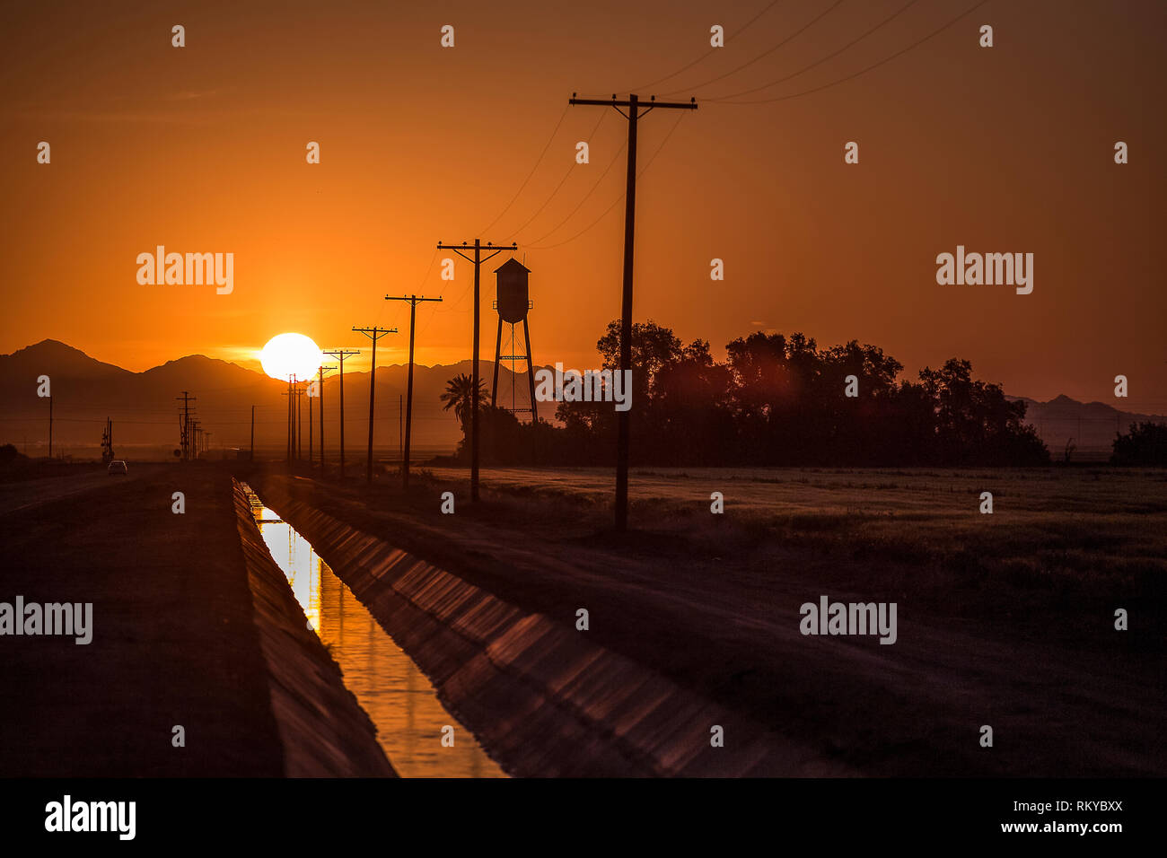 The sun rises behind a mountain and reflecting in an irrigation canal of an agricultural community. Stock Photo