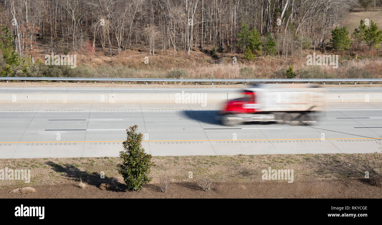 A red dump truck in blurred motion on a highway showing movement while the rest of the shot is in focus. Stock Photo
