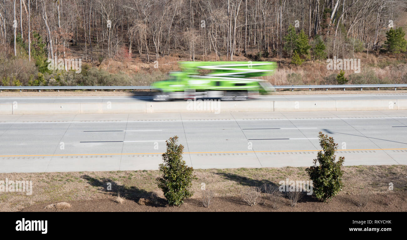 A green crane utility truck in blurred motion on a highway showing movement while the rest of the shot is in focus. Stock Photo