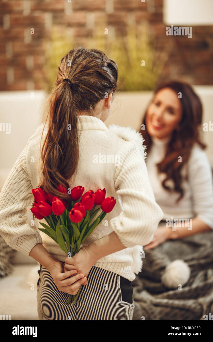 Little daughter is holding nice flowers for her amazed cheerful joyful charming mom congratulates mother's day to her. Stock Photo