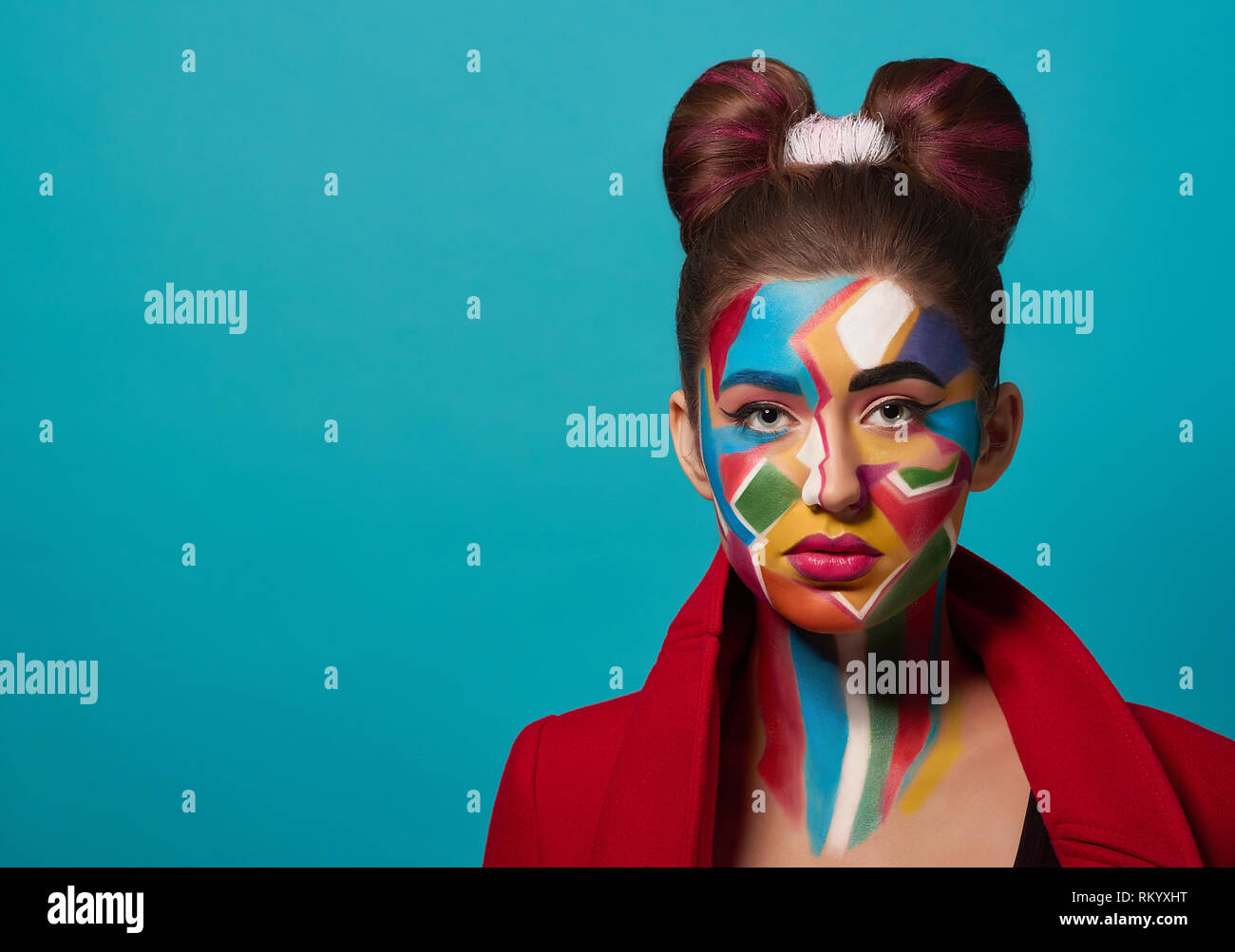 Portrait of funky girl with creative and colorful make up on face. Beautiful model wearing in red clothes, looking at camera, posing in studio. Woman has hairstyle bow, pink, plump lips. Stock Photo