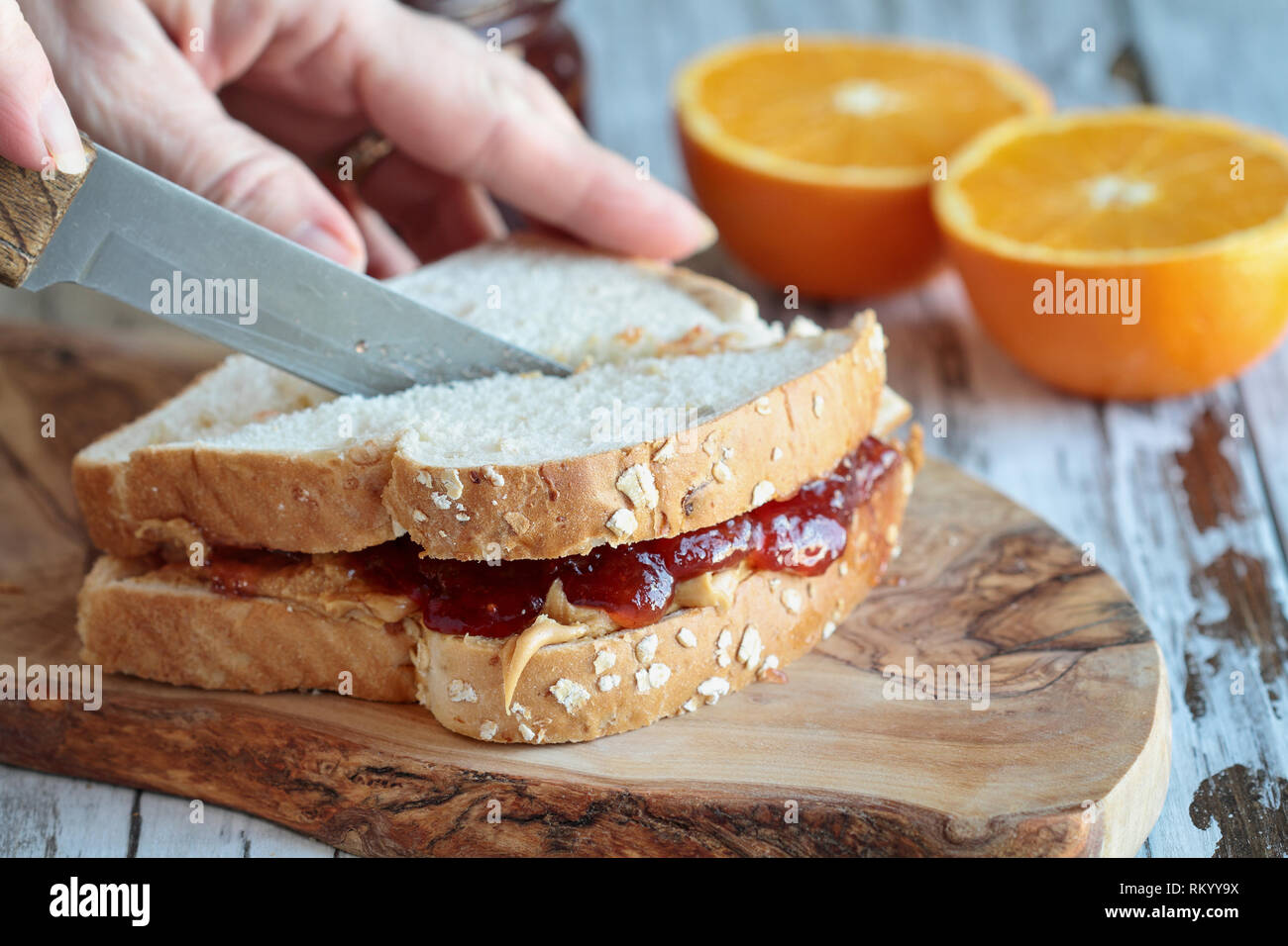Womans Hand Cutting A Peanut Butter And Jelly Sandwich On A Rustic