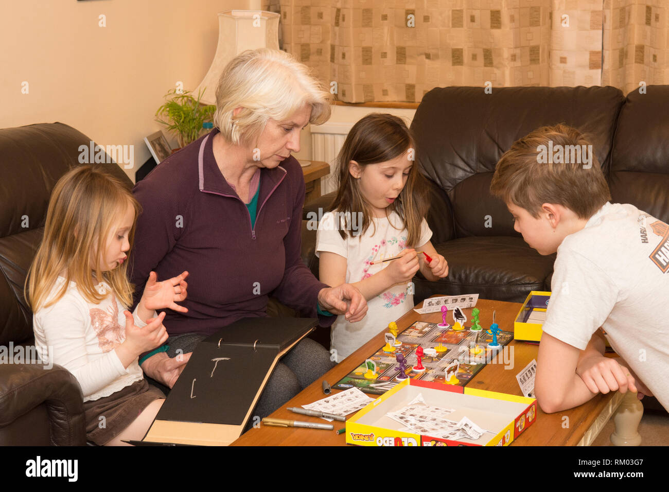 grandmother, granny, playing board game with three grandchildren, aged two to twelve, two girls, one boy. Stock Photo