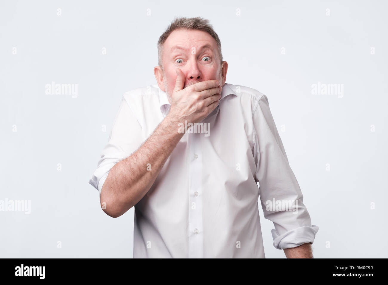 man in white shirt covering mouth with hand and looking at camera Stock Photo