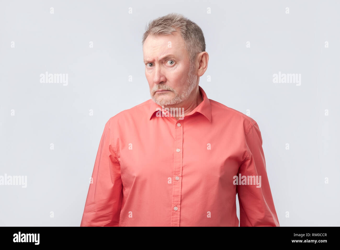 Senior man in red shirt frowning and squinting, showing disbelief or doubt Stock Photo