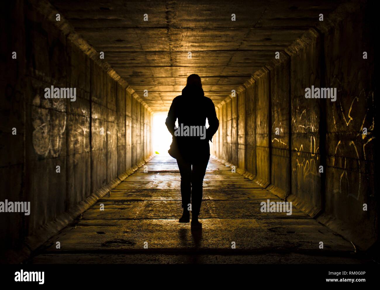 Female figure walking toward the light at the end of the tunnel Stock Photo