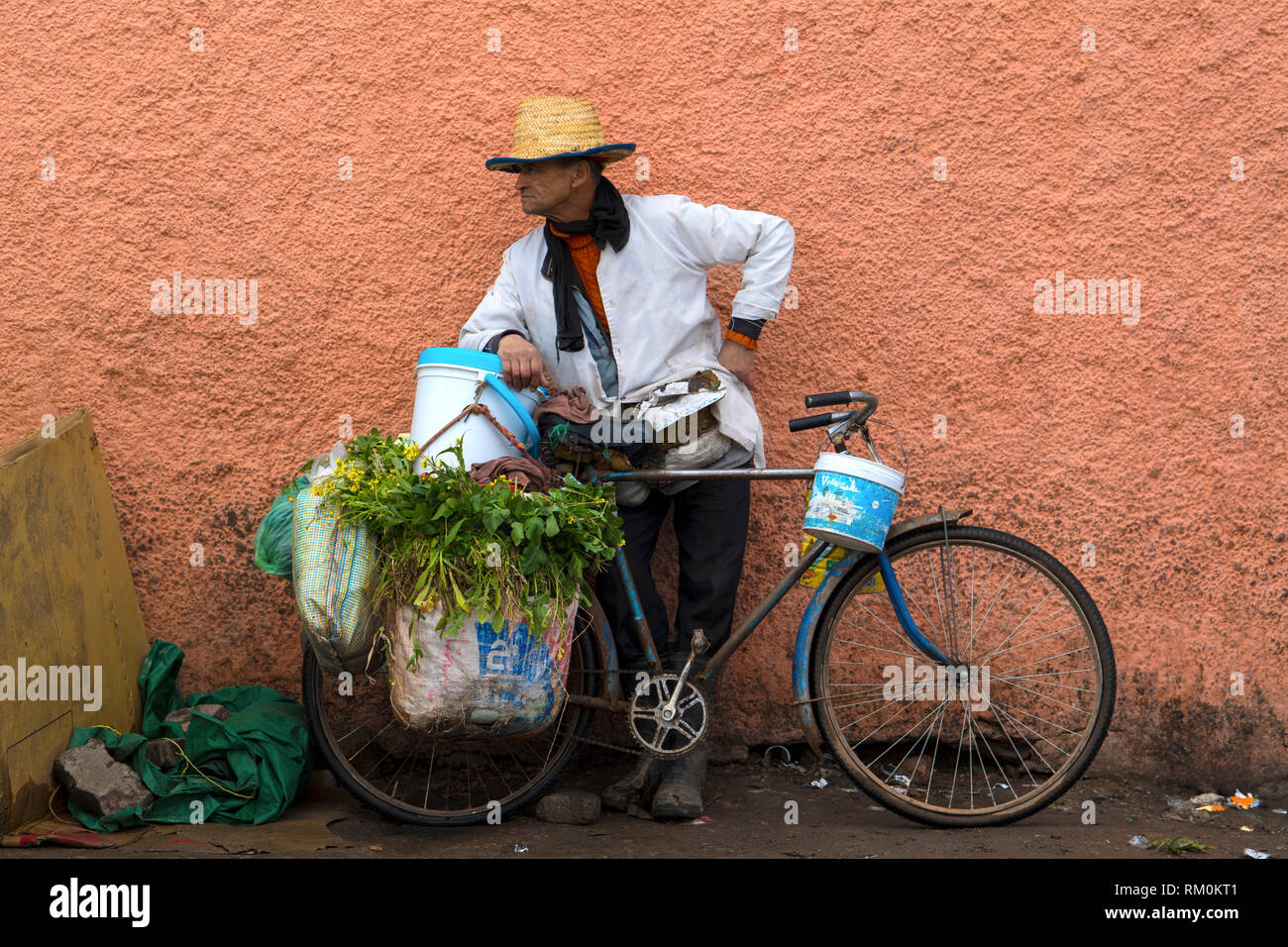 Old grumpy man selling vegetables and herbs from his old rusty blue bicycle in a Marrakesh food street market in Morocco. Stock Photo