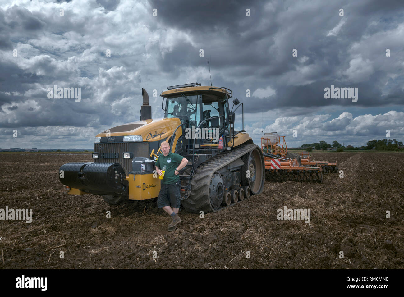 Young farmer ploughs his fields with huge challenger tractor and drilling rig. Stock Photo