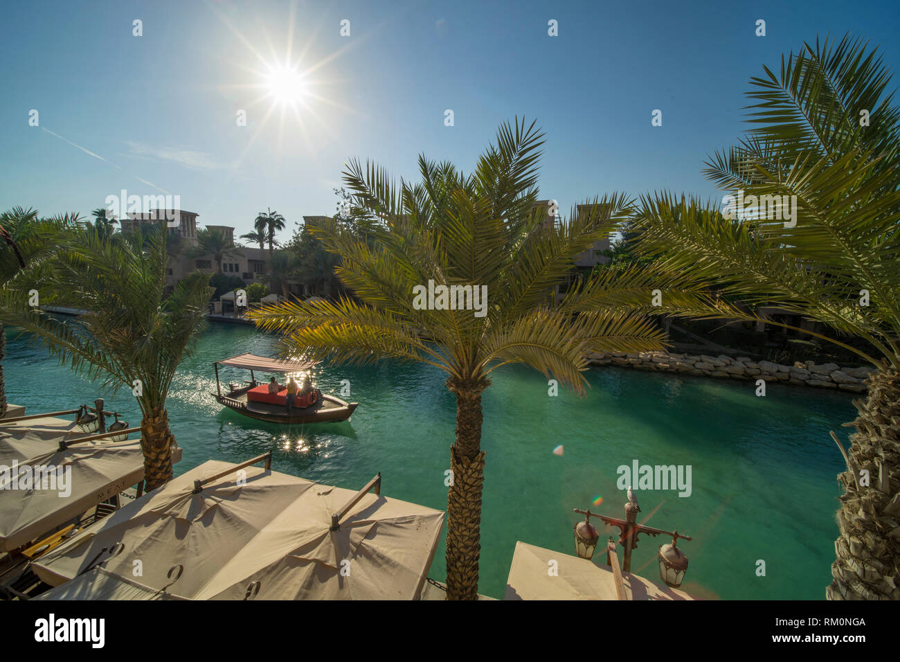 Canopied Arabian dhow makes its way down the blue waters of Souk Madinat Jumeirah and provides shade from the powerful desert sun in this lush oasis. Stock Photo