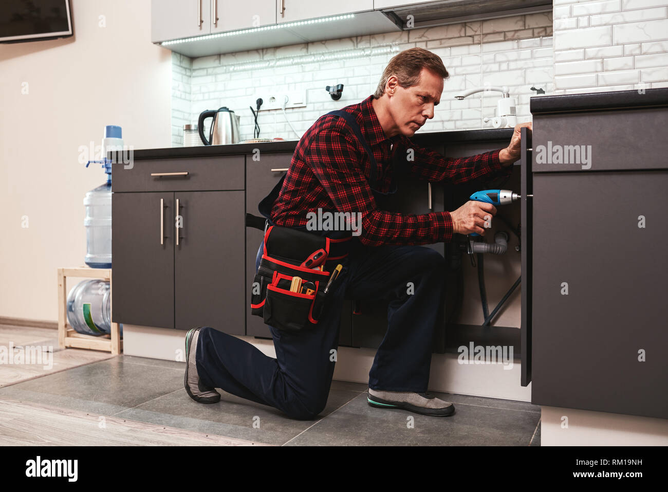 Handyman at work. Repairing kitchen shelves by perforator. Artisan
